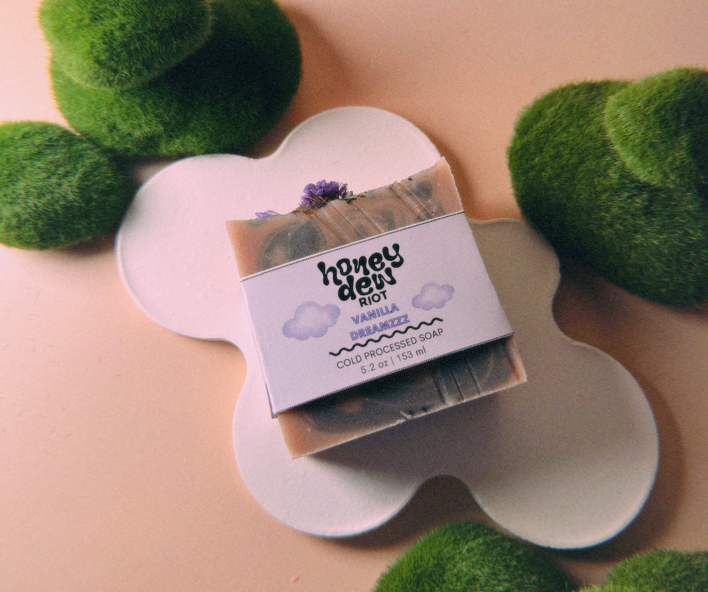 A bar of soap topped with lavender placed on a white cloud shaped stand surrounded by moss balls